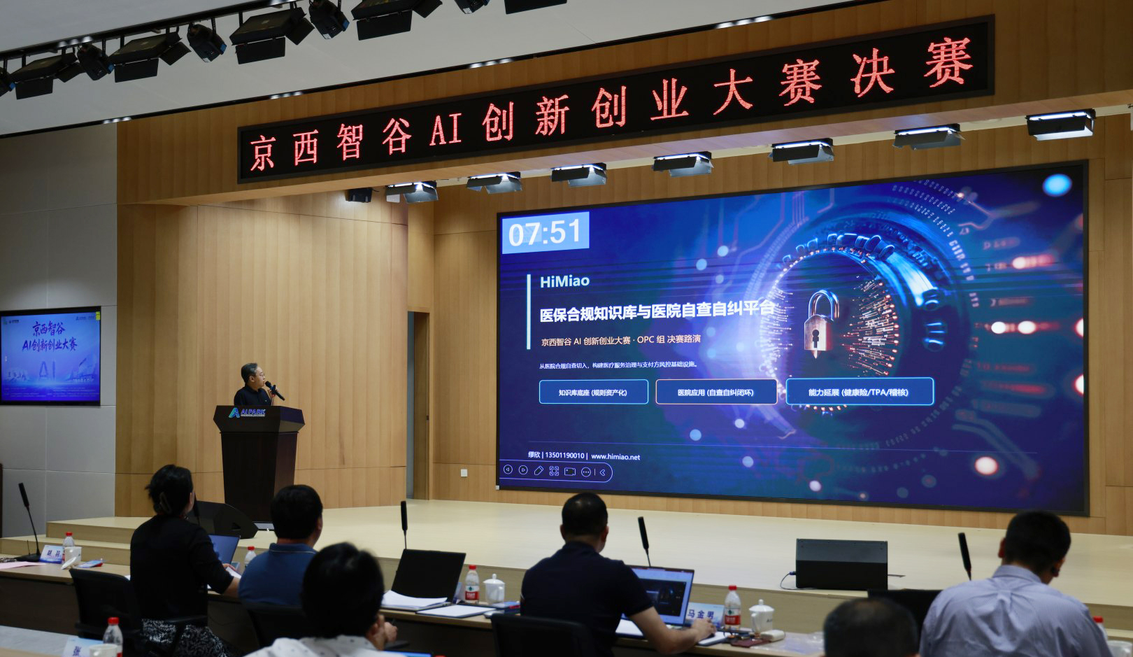 2026 京西智谷 AI 创新创业大赛决赛现场——HIMIAO 医保合规知识库项目路演，红色横幅 京西智谷 AI 创新创业大赛决赛